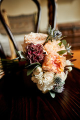 The bride’s wedding bouquet of natural roses and other plants lies on a wooden chair.