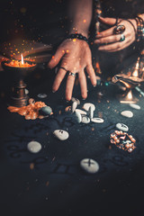 Astrology and esotericism. The witch's hands read the Runestones, throwing them forward. On a black background lie fortune-telling runes, amulets and a candle. Copy. Zodiac horoscope on the table