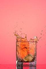 big splash from falling ice in a glass of whiskey on a red background