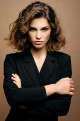 beauty fashion model with clean skin and curly hair in black jacket on biege background, serious business woman