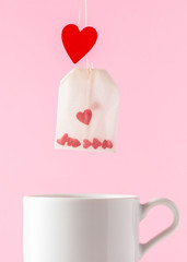 Valentines day concept. Tea bag with hearts inside and tea cup on the pink background.