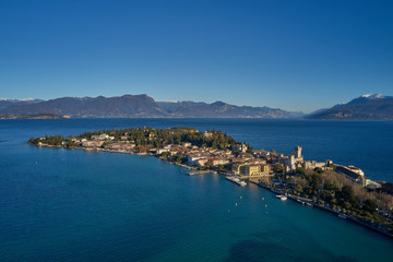 Naklejka na ściany i meble Unique view. Aerial photography, the city of Sirmione on Lake Garda north of Italy. In the background is the Alps in the snow. Resort place. Aerial view.Winter season