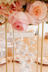 Beautiful Light Lamps in Glass Spheres and Flowers Roses on Metallic Skeleton Close-up Vertical Photography. Creative Ornament. Dishware Napkins on Plates and Wineglasses on Blurred Background