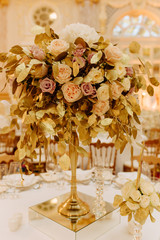 Decorative Bouquet Flowers Made from Rose Buds and Golden Leaves Branches Closeup Photography. Elegant Floral Ornament on Pedestal for Dinner Table. Luxury Restaurant Decor. Blurred Background