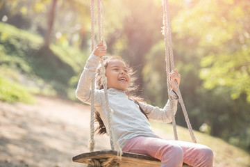 happy little asian girl child having fun to playing in the playground in summer time with smile and laughing healthy, Adorable girl having fun on a swing on summer. happy vacation lifestyle concept.