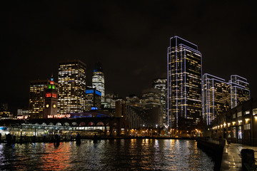 Naklejka premium San Francisco port illuminated at night, against the backdrop of impressive skyscrapers with light and reflection in the water, view from the side of the San Francisco Bay.