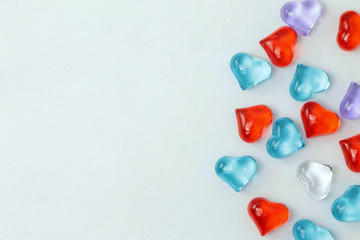 A scattering of glass hearts of blue, red, lilac and white on a white background. Stock photo for Saint Valentine's Day with empty place for text. For web, print, cards, invitations, wallpaper.