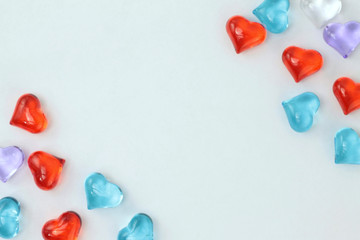 A scattering of glass hearts of blue, red, lilac and white on a white background. Stock photo for Saint Valentine's Day with empty place for text. For web, print, cards, invitations, wallpaper.