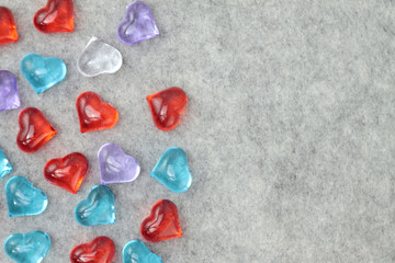 A scattering of glass hearts of blue, red, lilac and white on a gray felt background. Stock photo...