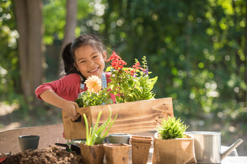 adorable asian little girl is planting spring flowers tree in pots in garden outside house, child...