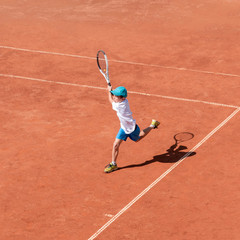 A boy plays tennis on a clay court. A little tennis player focused on the game and shot in flight...