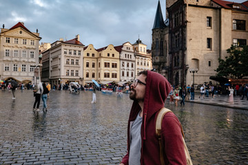 A man with a backpack and a red hoodie looks in surprise at the central square of the city of Prague.