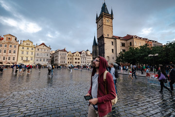 A man with a backpack and a red hoodie looks in surprise at the central square of the city of Prague.