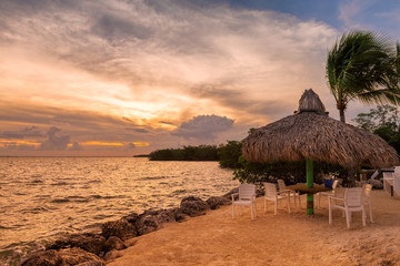 Tropical sandy beach at sunset with coco palms and beach umbrella with chairs in Key West, Florida.