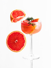 Cold lemonade of fresh grapefruit juice and ice cubes decorated a slice of grapefruit and twig rosemary, on the white isolated background. Copy space. Close up, selective focus. Near grapefruit slices