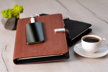 Two leather notebooks with built in power bank on wooden background with cup of coffe and green fresh moss. Set of diary with built in power bank in leather cover on wood table. Top view, copy space