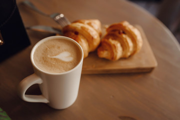 Cappuccino with beautiful latte art and croissant on wooden background