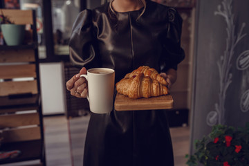 Close-up female hand serving hot latte and croissant in coffee shop.