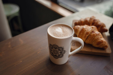 Cappuccino with beautiful latte art and croissant on wooden background