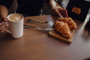 Close-up female hand serving hot latte and croissant in coffee shop.