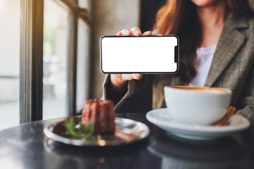 Mockup image of a woman holding and showing black mobile phone with blank screen with coffee cup and snack on the table in cafe