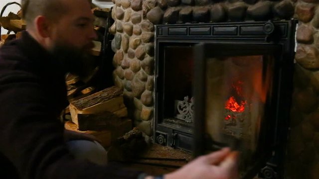 The man puts the wood into the firebox of the fireplace at his country house.
