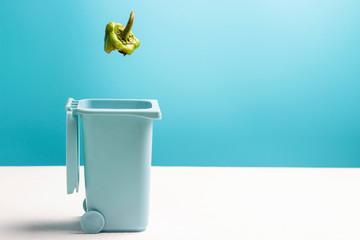Food waste falling in trash can on blue and white background, side view copy space.