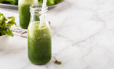 Blended green smoothie with ingredients on the white table.