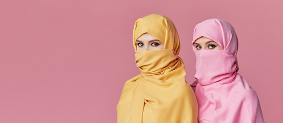 Girl power. Two young Muslim arabian women wearing colorful hijabs against pink background. Points...