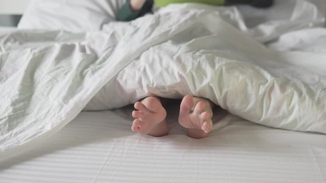 White Baby Feet Are Moving Under a Blanket. Close-up of the boy's feet in a white bed