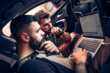 Mechanics using laptop on car at repair garage