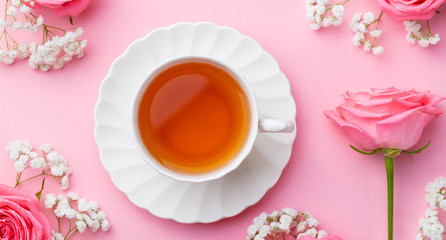 Cup of tea with fresh flowers on pink background. Copy space. Top view.