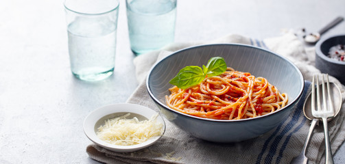 Pasta, spaghetti with tomato sauce and fresh basil in a bowl. Grey background. Copy space.