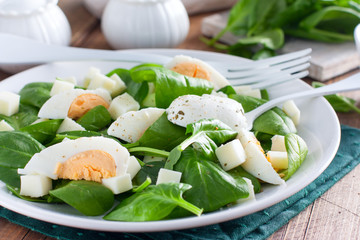 Spinach, egg and cheese salad on a white plate on a wooden table, selective focus