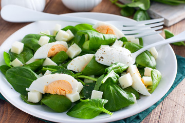 Spinach, egg and cheese salad on a white plate on a wooden table, selective focus