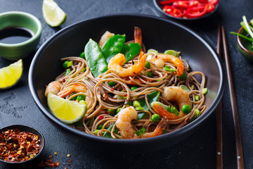 Stir fry noodles with vegetables and shrimps in black bowl. Slate background. Close up.