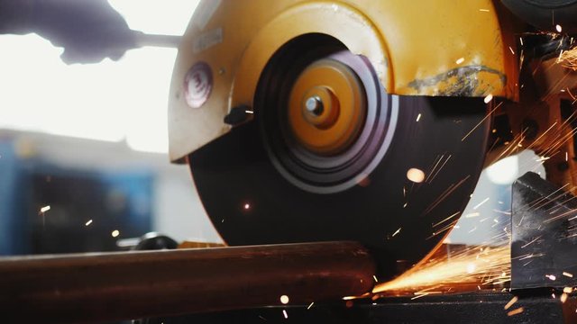 worker cuts metal pipe with saw at production plant closeup