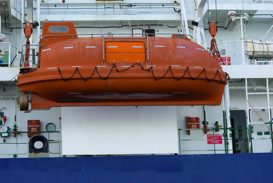 Enclosed safety orange life boat launching on the cargo ship during ship drill. 