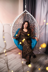Fat plump charming cute woman with black curly hair in black beautiful dress in a white wicker chair