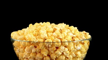 Transparent glass bowl with yellow popcorn filled to the top on a black background