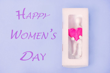 Greeting card for Women's Day. In a box with a transparent top, there is a figure of a man from white plasticine holding a heart in his hands..