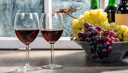 two wineglasses, red and white grapes with bottles of red wine