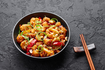 Kung Pao Cauliflower at dark slate background. Sichuan Kung Pao Cauliflower is chinese cuisine vegetarian dish with chilli peppers, peanuts, sauces and onion. Copy space