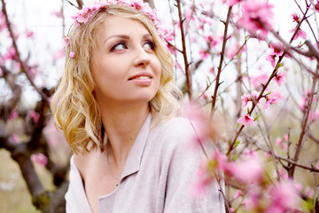 Fototapeta premium portret pięknej kobiety w ciąży pozowanie na tle różowych drzew kwiatowych ogród i mgła wiosną, ubrany kardigan w proszku i wieniec różowy kwiat. Kobieta trzyma brzuch.