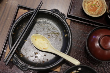 A dirty black plate, spoon and chopsticks.
