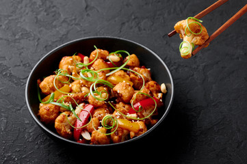 Kung Pao Cauliflower at dark slate background. Sichuan Kung Pao Cauliflower is chinese cuisine vegetarian dish with chilli peppers, peanuts, sauces and onion.
