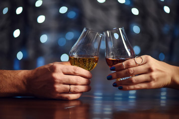 A couple makes a toast with two glasses of whiskey on festive background