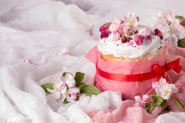 Happy Easter decoration for greeting card. Easter cake with white icing, marshmallows, dry rose and fresh blooming apple flowers and rose color craft paper on gauze background..