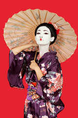 Portrait of Japanese woman in kimono holding parasol against red background
