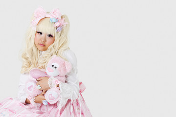 Fototapeta premium Portrait of cute woman dressed as a doll holding soft toy over gray background